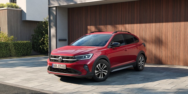 Roter VW Taigo ENERGY parkend vor modernem Garagentor aus Holz.