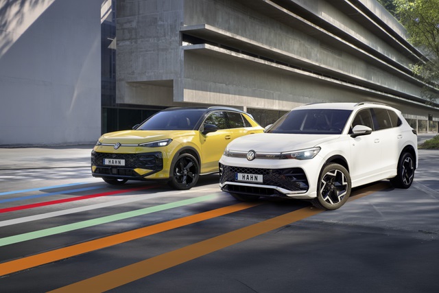 Gelber VW T-Roc R-Line und weißer VW Tiguan R-Line stehen nebeneinander vor einem Gebäude.