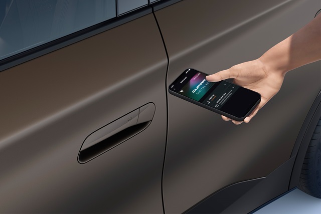 Hand hält Smartphone mit geöffneter Cupra-App vor Türgriff eines beigen Fahrzeugs.