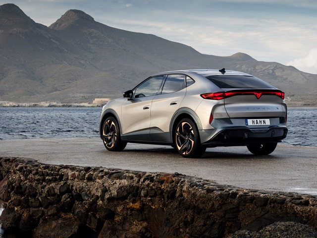 CUPRA Tavascan in der Rückansicht steht auf einer Klippe, im Hintergrund Wasser und Berge