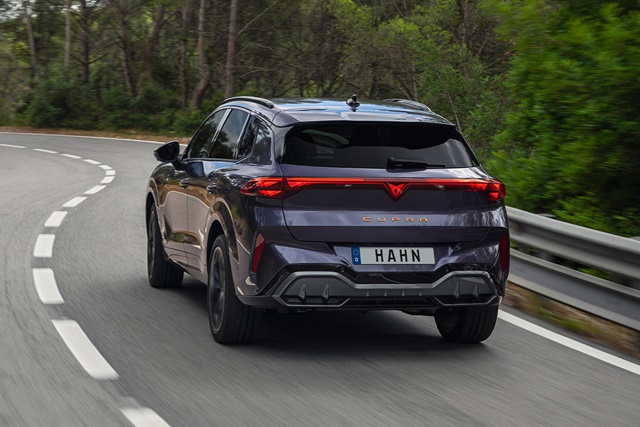 Heckansicht eines dunkelvioletten CUPRA Terramar SUV mit dem Kennzeichen 'HAHN' auf einer kurvigen Landstraße mit Wald im Hintergrund