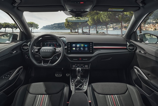 Innenraum des Škoda Fabia 130 mit Lenkrad, digitalem Kombiinstrument, großem mittigem Touchscreen, Schalthebel und zwei Vordersitzen vor einer Küstenlandschaft
