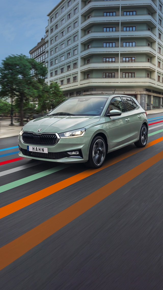Škoda Fabia in Grün fährt auf einer Straße in urbaner Umgebung mit modernen Gebäuden im Hintergrund
