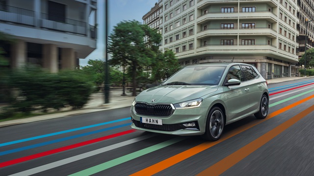Škoda Fabia in Grün fährt auf einer Straße in urbaner Umgebung mit modernen Gebäuden im Hintergrund