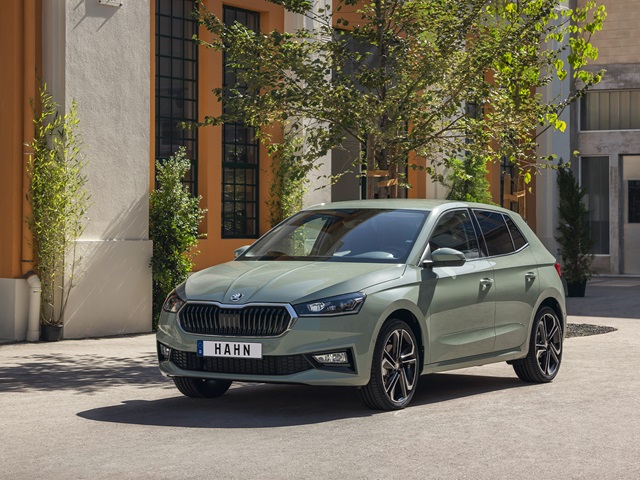 Hellgrüner Škoda Fabia in Frontansicht vor einem Gebäude mit orangefarbenen und weißen Wänden und Bäumen im Hintergrund