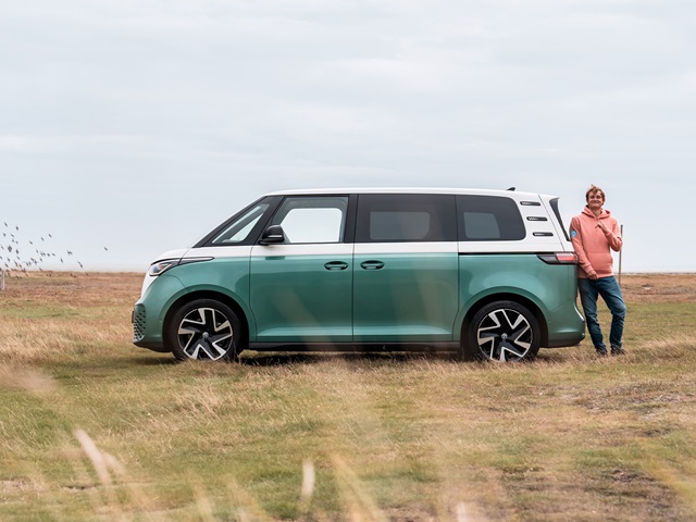 VW ID. Buzz in grün-weiß seitlich fahrend auf einem unbefestigten Weg in einer offenen Landschaft
