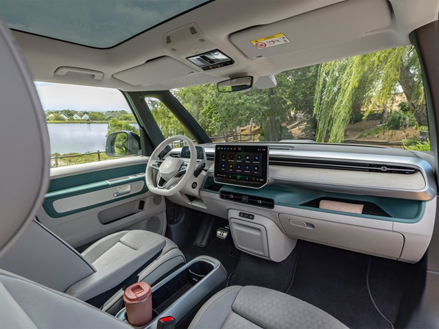 Innenraum des VW ID. Buzz mit modernem Armaturenbrett, großem mittigem Touchscreen, hellgrauen Sitzen und grünem Dekor an Tür und Armaturenbrett