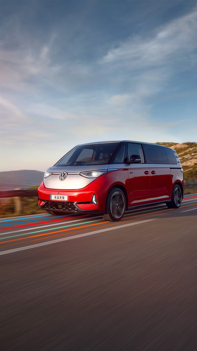 Roter VW ID. Buzz fährt auf einer Landstraße mit bewölktem Himmel im Hintergrund