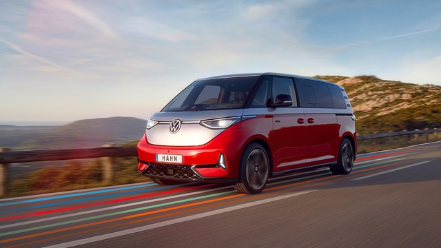 Roter VW ID. Buzz fährt auf einer Landstraße mit bewölktem Himmel im Hintergrund