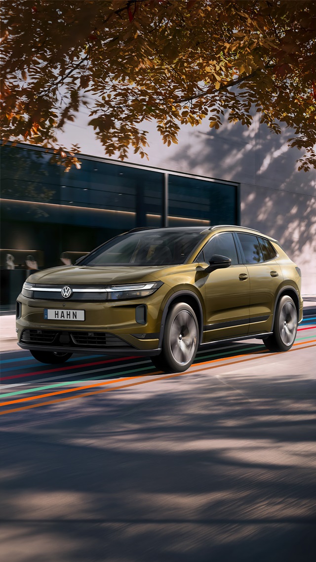 Bronzefarbener VW ID. Tiguan in Frontansicht vor modernem Gebäude mit Schatten von Baumblättern
