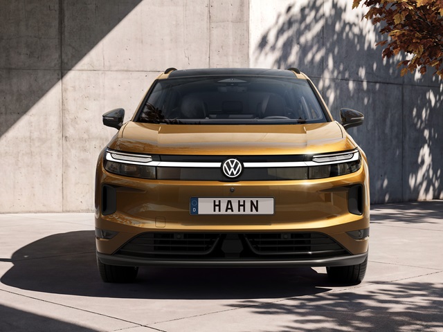 Bronzefarbener VW ID. Tiguan in Frontansicht vor einer Betonwand mit Schatten von Bäumen