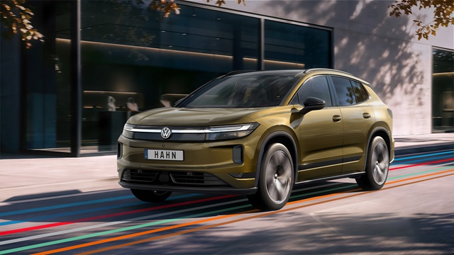 Bronzefarbener VW ID. Tiguan mit schwarzem Dach und markantem LED-Lichtband in Frontansicht auf Straße vor modernem Gebäude