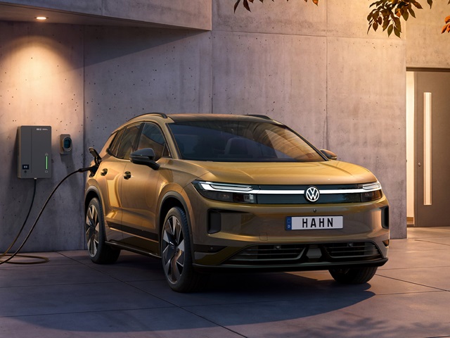 Bronzefarbener VW ID. Tiguan steht an einer Ladestation vor einer modernen Betonwand mit beleuchtetem Türrahmen