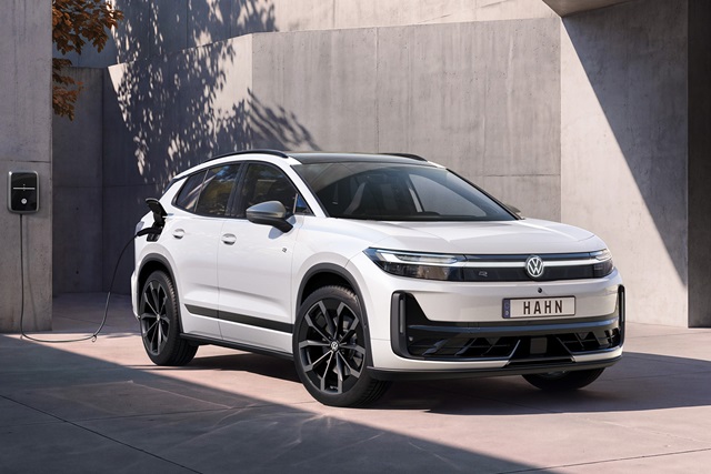 Weißer VW ID. Tiguan mit schwarzem Dach und schwarzen Felgen, an einer Ladestation stehend, Frontansicht vor grauer Betonwand