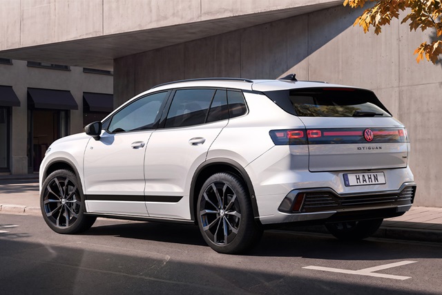 Weißer VW ID. Tiguan von hinten rechts mit schwarzem Dach und schwarzen Felgen vor einer Betonwand