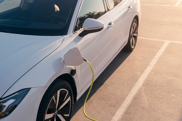 Weißer Pkw mit Ladekabel an der Vorderseite auf einem Parkplatz