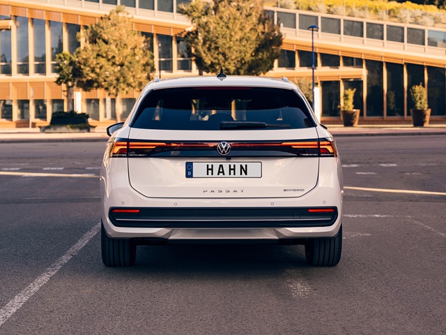 Weißer VW Passat aus der Rückansicht mit breitem LED-Leuchtenband und dem Kennzeichen 'HAHN' auf einem freien Parkplatz