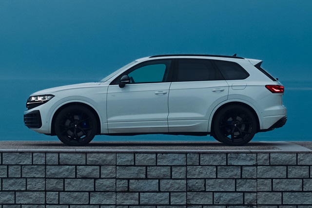 Weiße Seitenansicht eines VW Touareg R e-hybrid mit schwarzen Felgen auf einer Steinmauer vor blauem Himmel