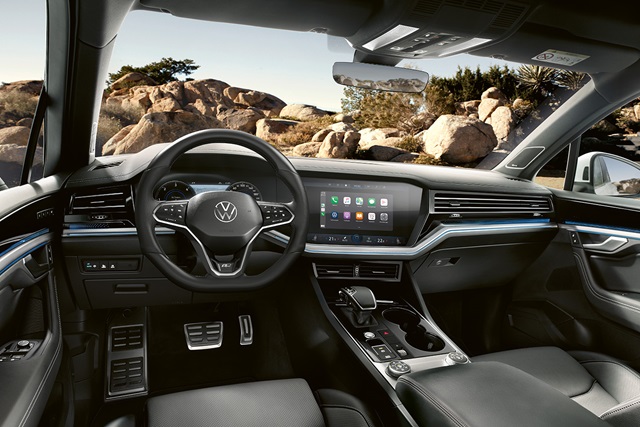 Innenraum eines VW Touareg R-Line mit digitalem Cockpit, großem Touchscreen und schwarzem Lederlenkrad vor felsiger Landschaft