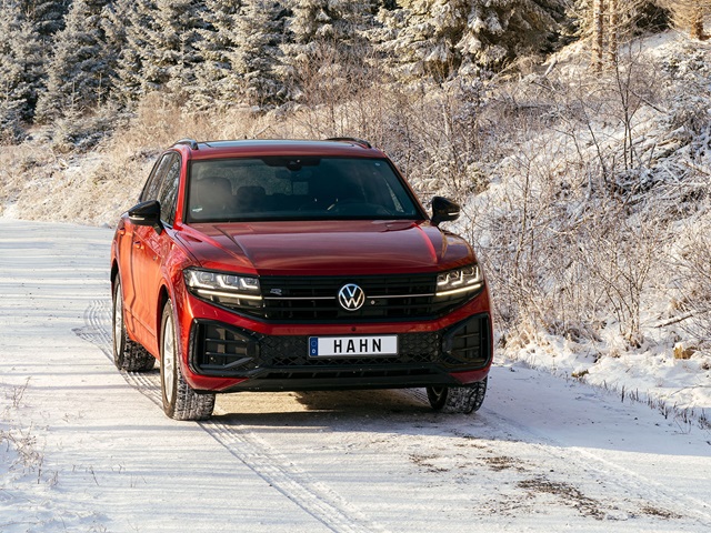 Roter VW Touareg R-Line steht auf verschneiter Straße vor winterlicher Waldkulisse