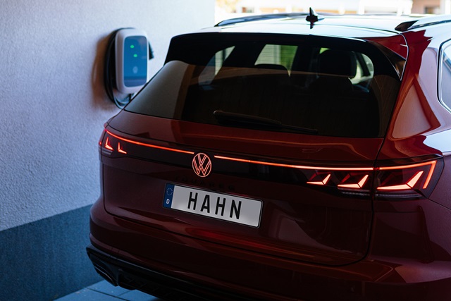 Rote Heckansicht eines VW Touareg R-Line mit leuchtenden Rücklichtern und Kennzeichen 'HAHN' beim Laden an einer Wandladestation