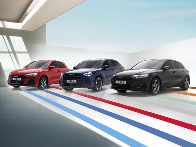 Drei Audi Modelle in einer modernen Umgebung. Die Autos stehen auf einem hellen Boden mit bunten Streifen.