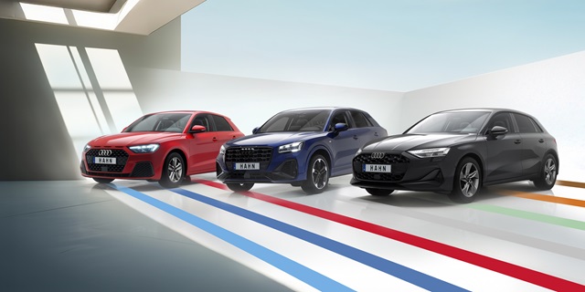 Drei Audi Modelle in einer modernen Umgebung. Die Autos stehen auf einem hellen Boden mit bunten Streifen.